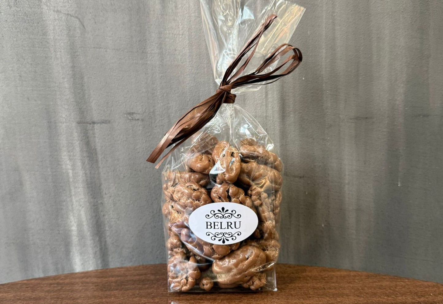 Clear cellophane bag with brown ribbon containing nuts on a wooden surface with a gray background
