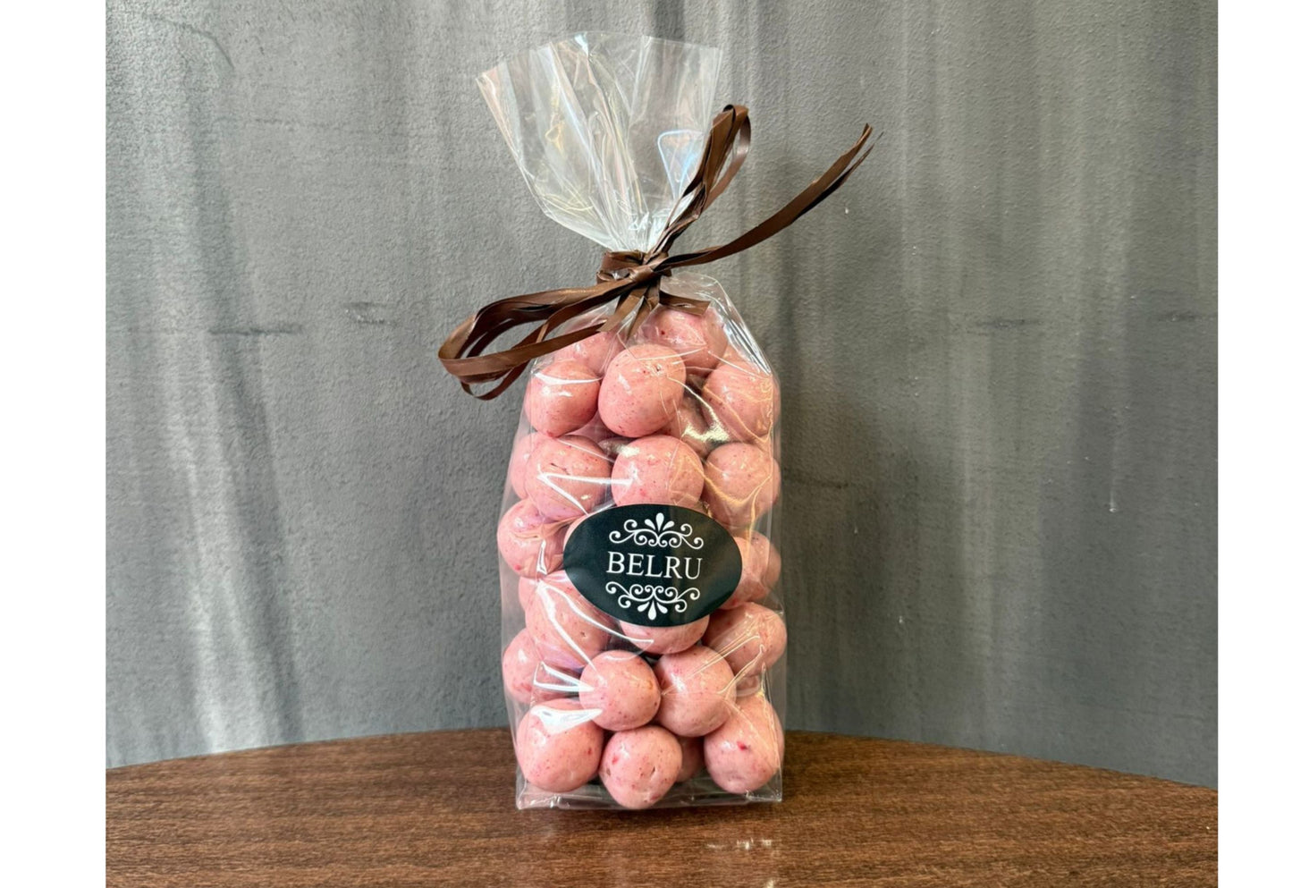 Bag of pink candies with a visible brand label on a wooden surface and gray background